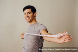 Smiling Hispanic male holding measuring tape out in front of him in beige studio shoot 0yoMq4