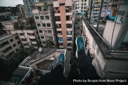 Person in dark pants and blue sneakers sitting on top of building 5pDNA5
