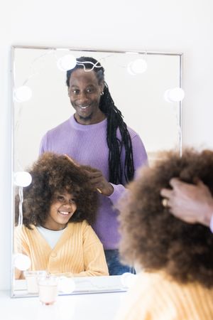 Black man brushing curly hair of smiling daughter