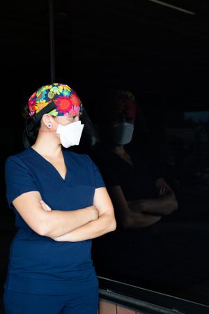 Portrait of woman nurse in PPE with arms crossed looking into dark window