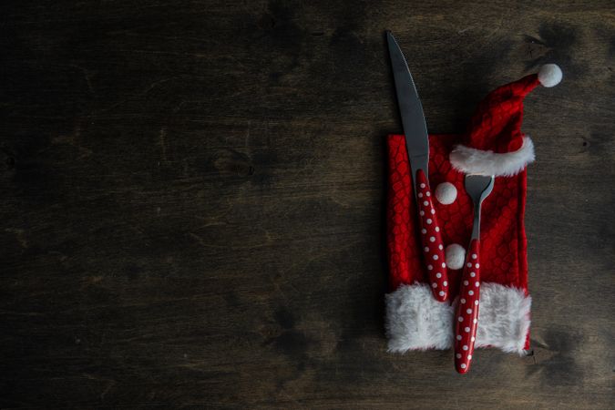 Cutlery setting with red Santa hat on silverware on rustic background