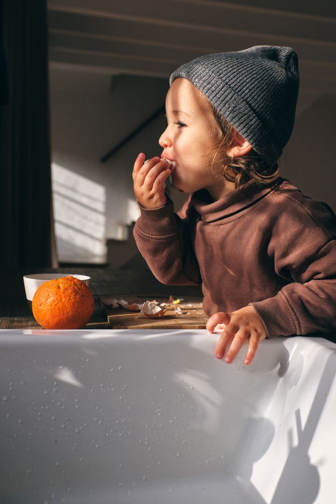Hungry toddler eating fresh orange in kitchen