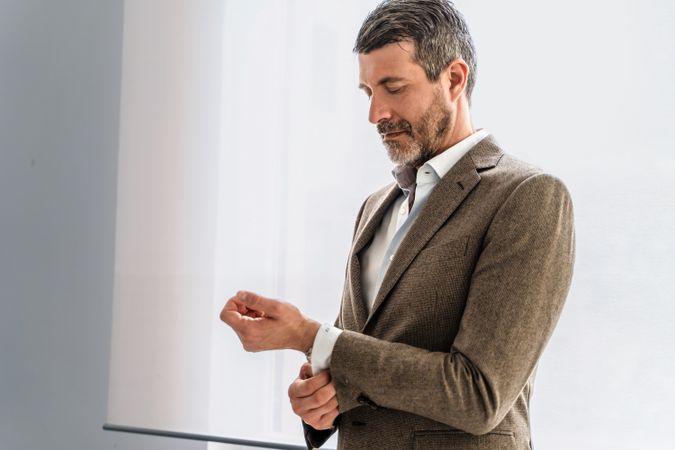 Mature businessman meticulously adjusting his shirt cuff, detailing attention to professional appearance