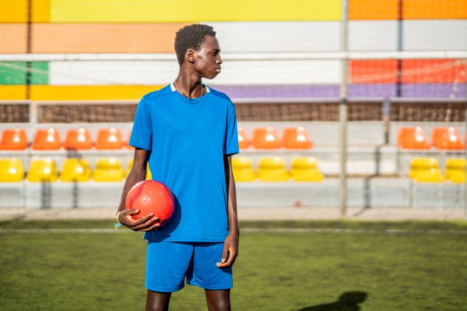 Black football player with ball standing on stadium