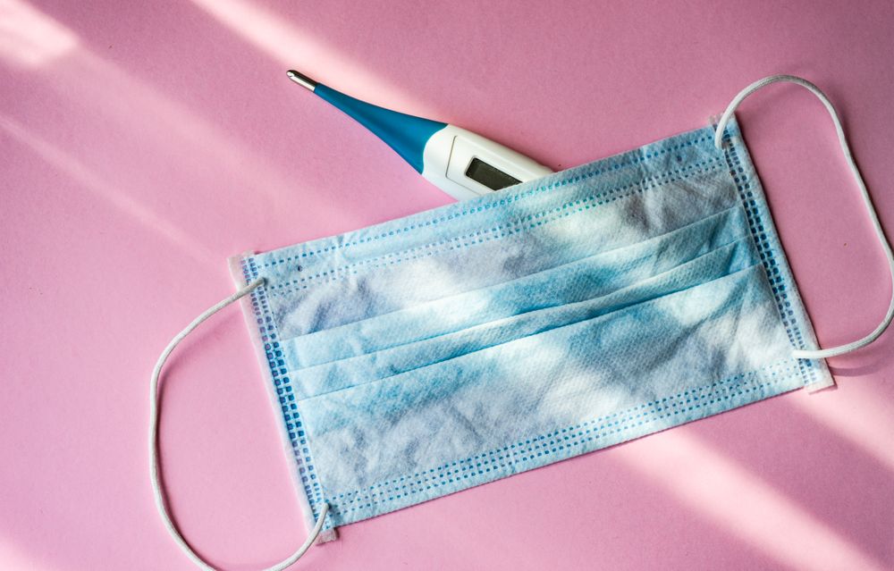 Looking down at pink table with facemask and digital thermometer