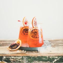 Two glasses of an orange cocktail with blood orange slices, and cocktail picks