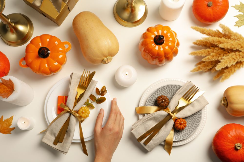Golden cutlery on plates, pumpkins and hand on light background, top view