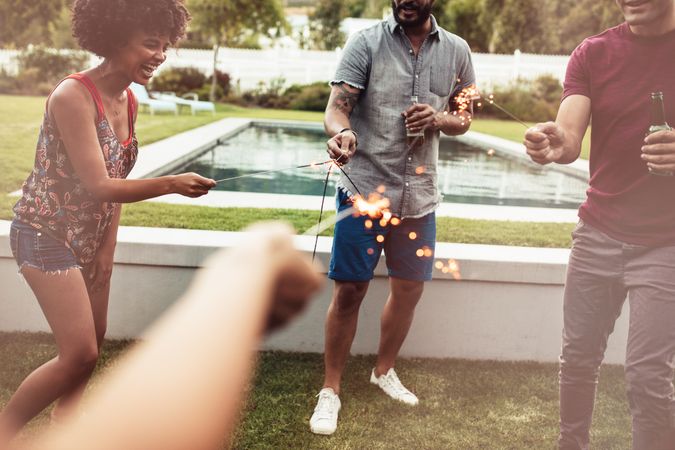 Cropped shot of group of friends lighting sparklers in backyard