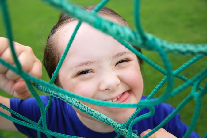 Close up portrait of little girl looking at camera framed by playground net