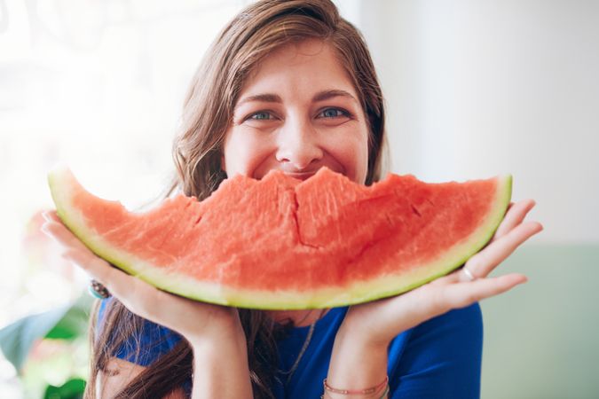 Playful woman holding watermelon near her face