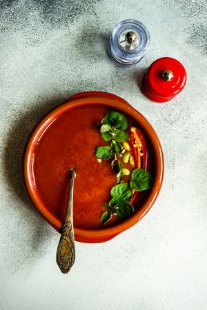 Top view of tomato soup in ceramic bowl with salt and pepper grinder