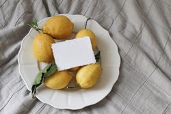 Fresh yellow lemons, dry green leaves on plate with blank card