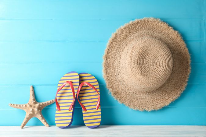 Flip flops, straw hat and starfish on table against color wooden background, space for text. Summer vacation backdrop