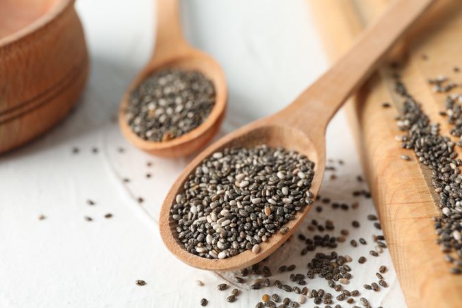 Wooden spoons with chia and board on plain background, close up