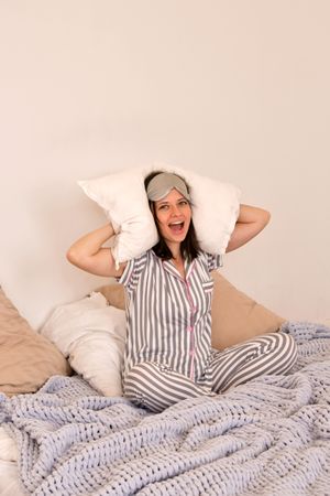 Woman in pajamas laughing with pillows behind her head.