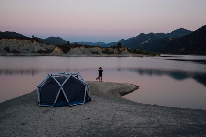 Man and dog looking over lake with tent at sunset