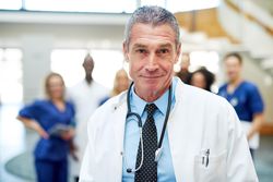 Portrait of mature doctor in lab coat and stethoscope with his team in the background
