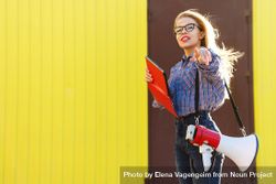 Woman pointing dressed in checkered shirt against a yellow wall 5zO2X4