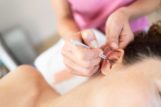 Crop masseuse applying flexible massage ear pen during auriculotherapy tr in salon