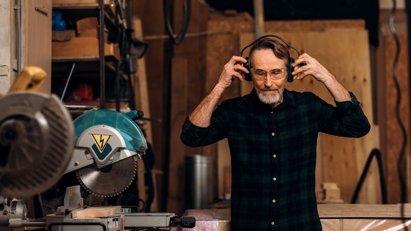 Older man putting on hearing protection on tablet in his woodwork shop