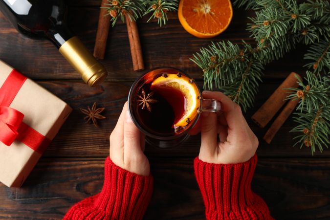 Girl holding glass with mulled wine on decorated wooden background, top view