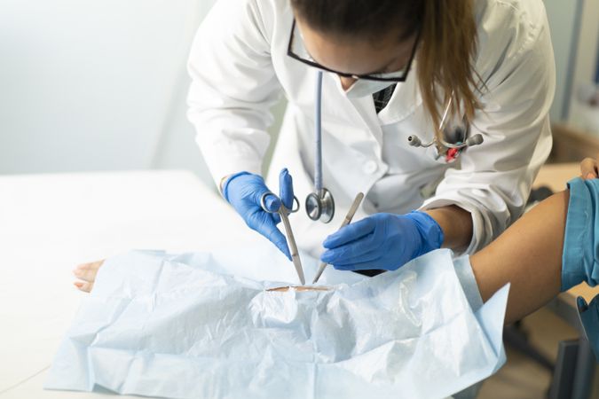 Young doctor with scissors and tweezers near hand of patient