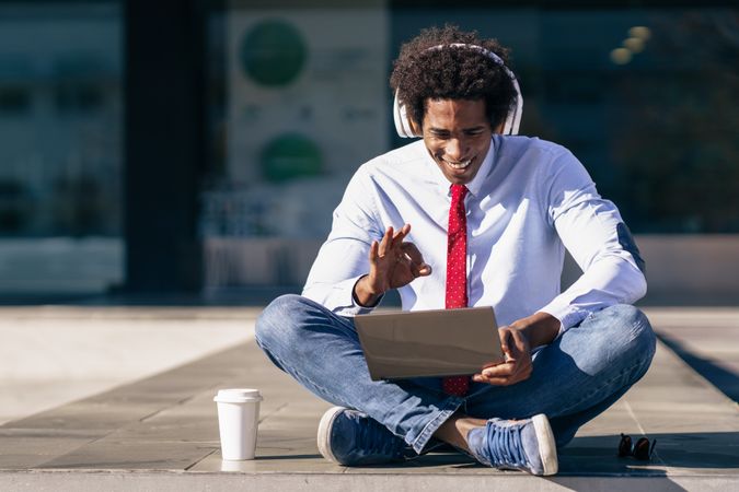 Man sitting crosslegged outside with laptop, coffee and headphones