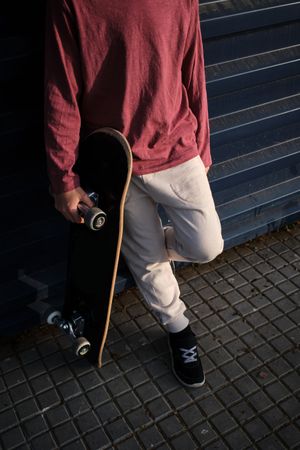 Crop skater leaning on wall on city street