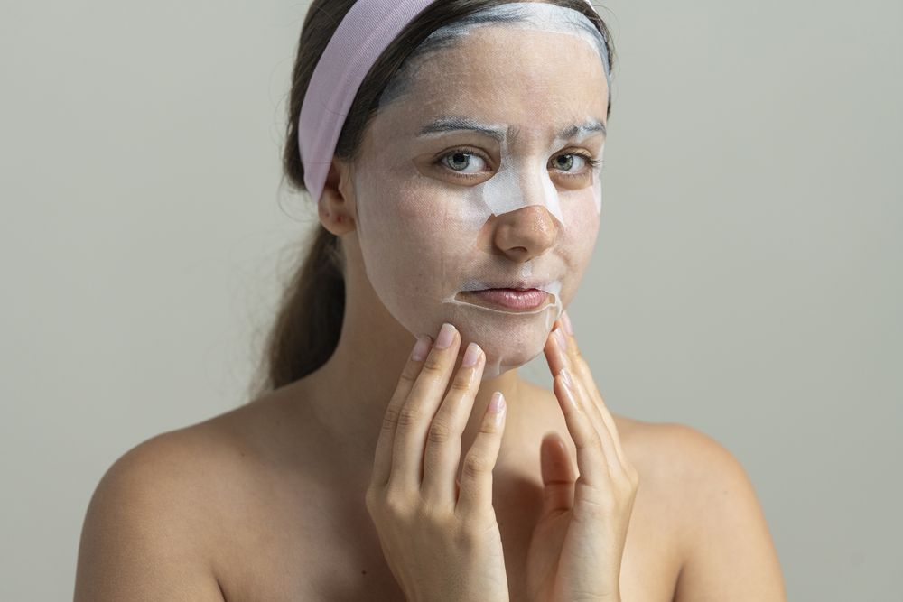 Young woman looking at camera while wearing a hydrating sheet mask for a home spa facial