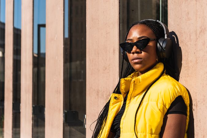 Black woman listening to music while leaning on a wall
