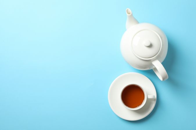 Cup of tea and teapot on blue background, space for text