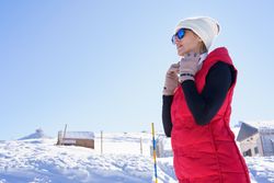 Low angle of female in warm clothes and sunglasses putting on headphones on snowy terrain