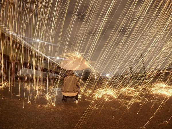 Man kneeling on ground under illusion of steel wool raining outdoor