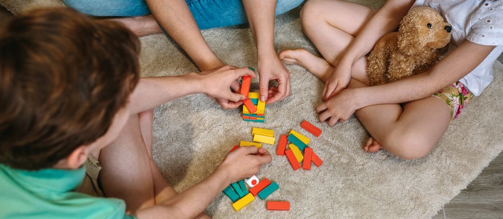 Banner of unrecognizable mother and sons having fun playing wooden stacking piece game at home