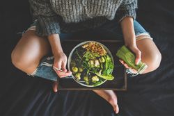 Woman in jeans sitting crosslegged with wooden tray of vegetarian bowl with smoothie on side