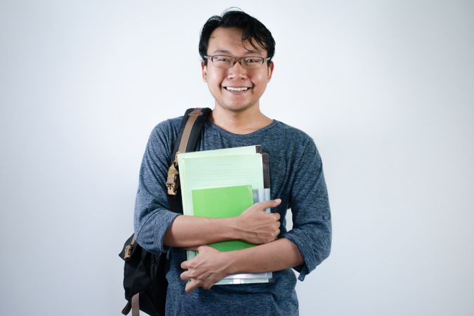 Asian young male student wearing bag and carrying books smiling and happy expression