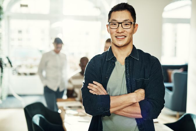 Portrait of Asian man smiling with arms crossed in bright office, landscape