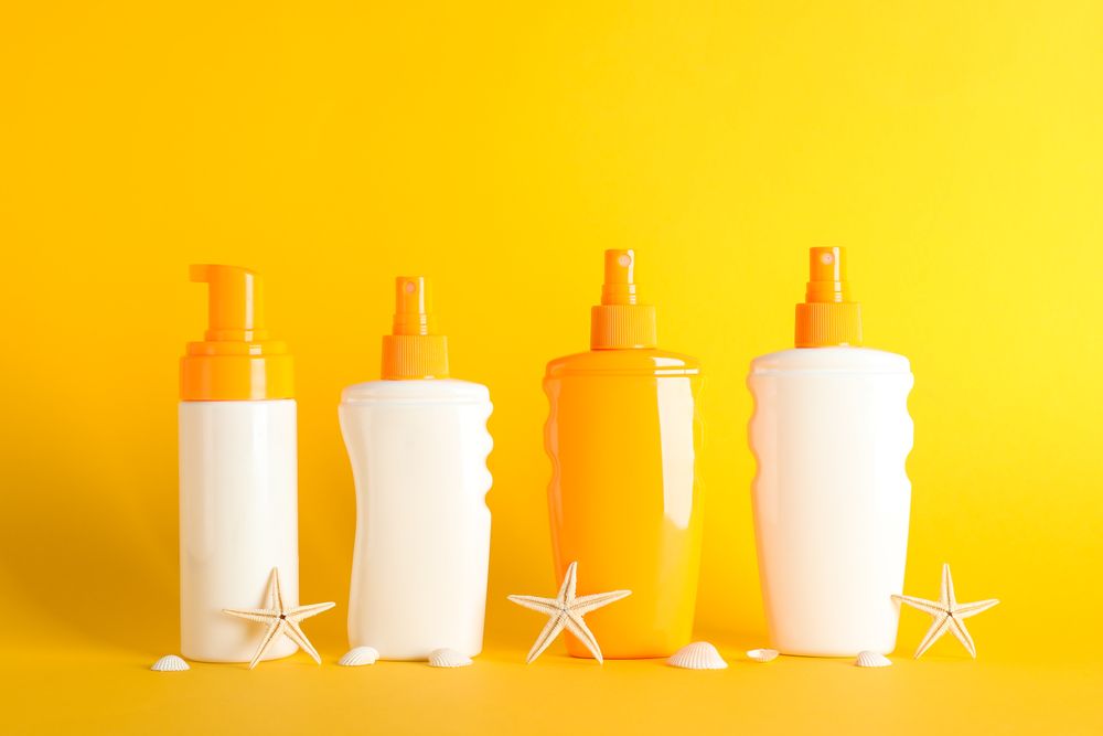 Sunscreen sprays with starfishes on color background, space for text. Safe tan accessories