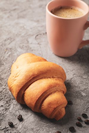 Croissant and pink mug of coffee on grey table, vertical composition