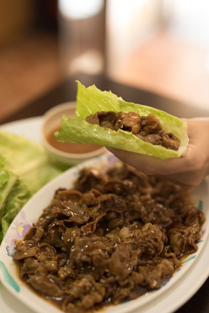 Hand holding meat wrapped in lettuce in restaurant