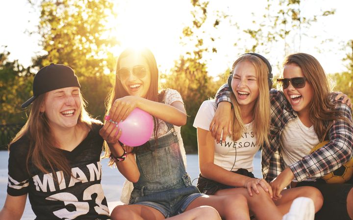 Group of female teenagers with a balloon and earphones in the sun