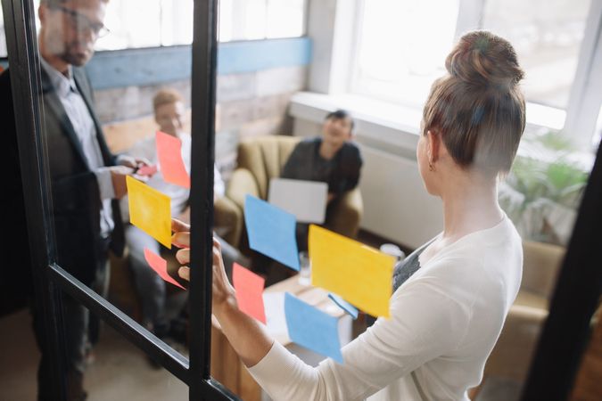 Woman standing in front of glass wall with post it notes and talking to colleagues