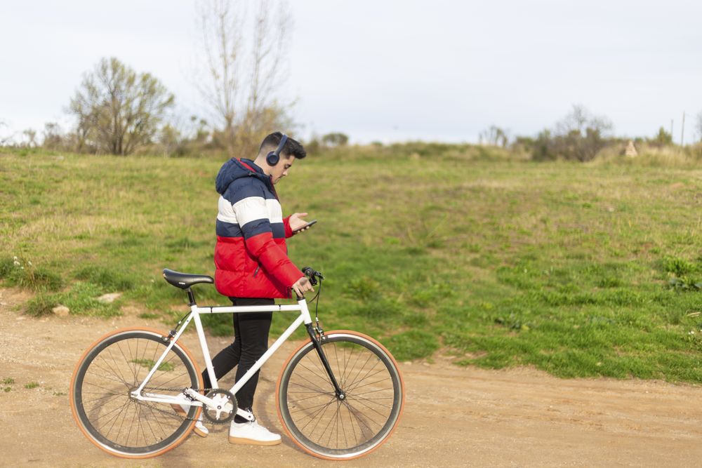Side view of man using a smartphone while walking with bike in park