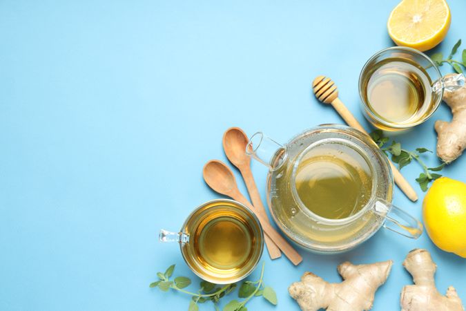 Cups and teapot with tea, lemon, ginger on blue background, space for text