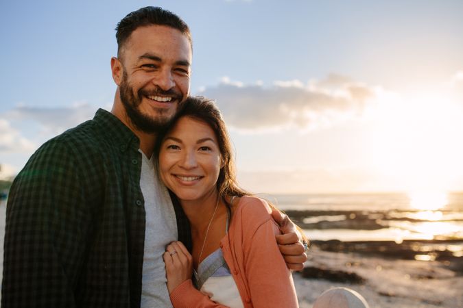 Portrait of cheerful couple embracing by the sea side at dusk