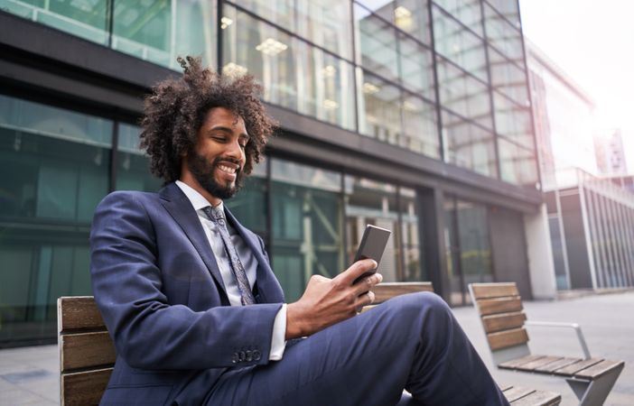 Joyful man in suit sitting outside and messaging