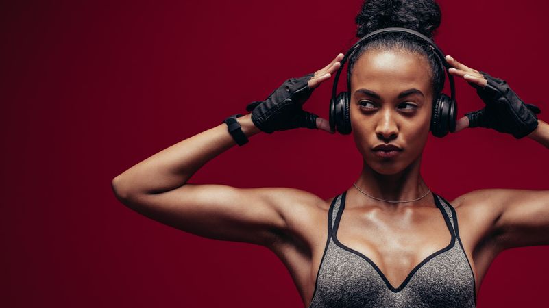Muscular Black female with headphones on red background