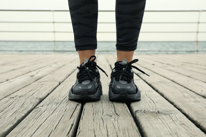 Female legs in leggings and sneakers on wooden floor outdoors, close up
