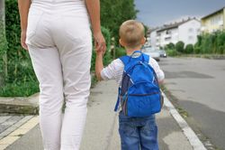 Unrecognizable boy with backpack walking on street with mother