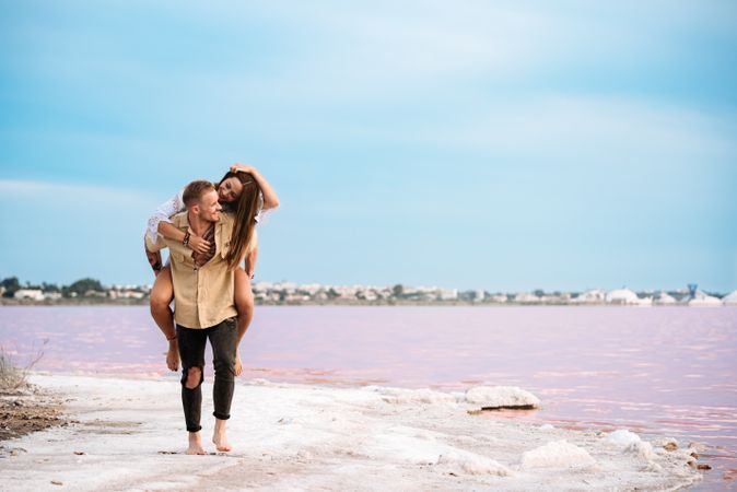 adorable couple giving a piggyback ride on an amazing beach of pink water